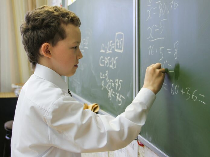 The boy is studying at school. A child stands at the blackboard in a math lesson and solves a math